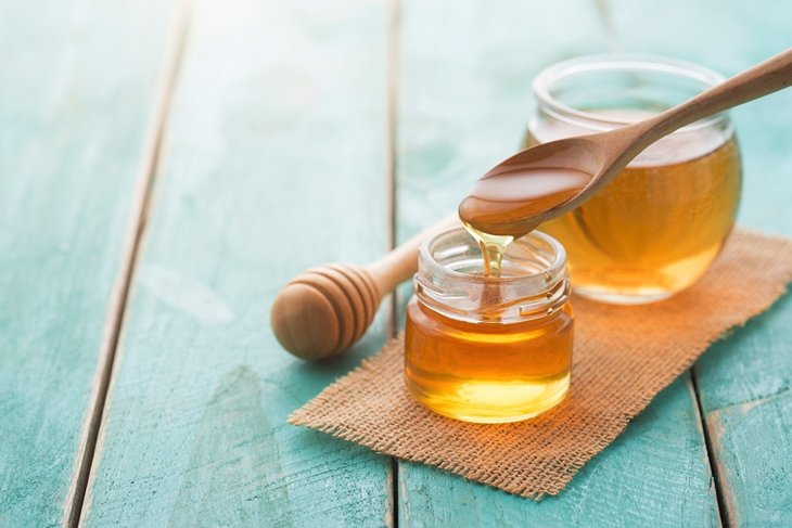 Honey with wooden honey dipper on blue wooden table