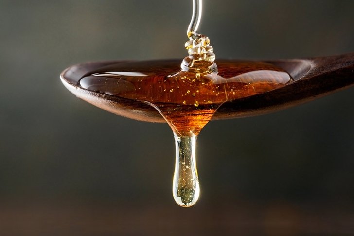 Honey pouring on wooden spoon and dripping from spoon. Dark background. Extreme close up