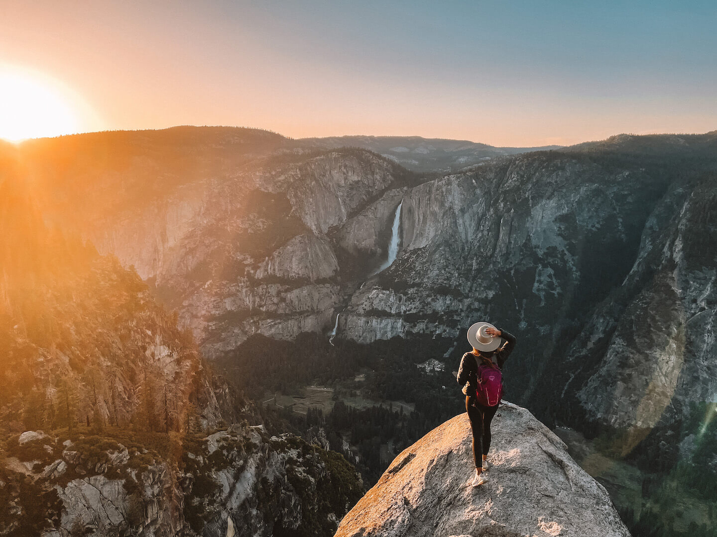 Nabila Ismail stands at the edge of a rock ledge overlooking a canyon view as the sun sets ahead of her